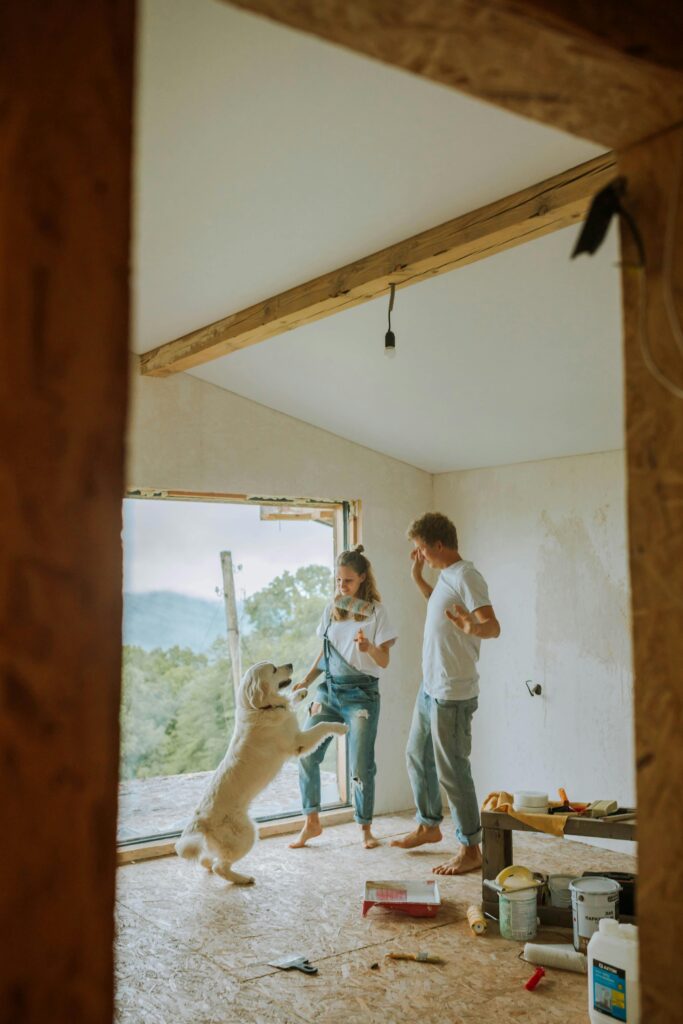 Happy couple and dog renovating their home, enjoying a playful moment indoors.